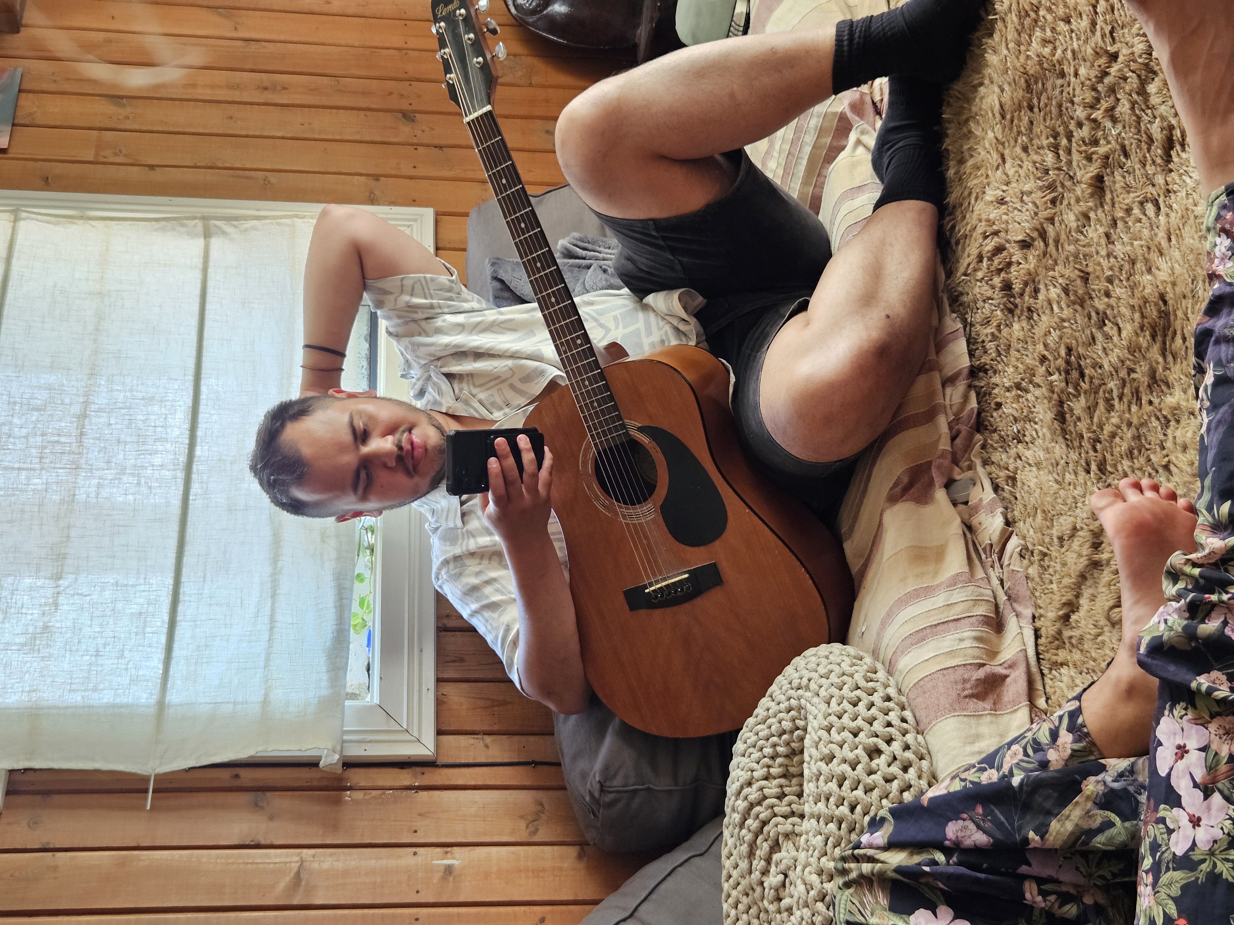 Person som sitter avslappet i koselig trerom med akustisk gitar