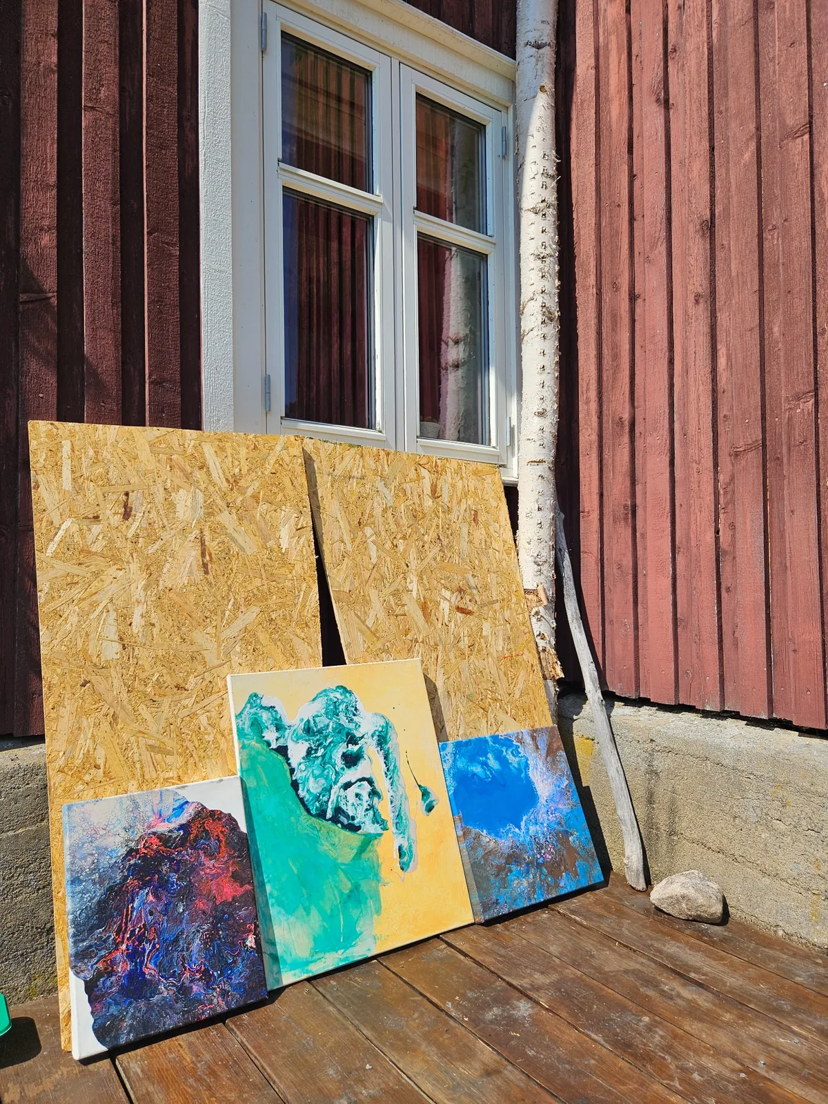 Tre abstrakte malerier lent mot rød trevegg ved Rennehøl