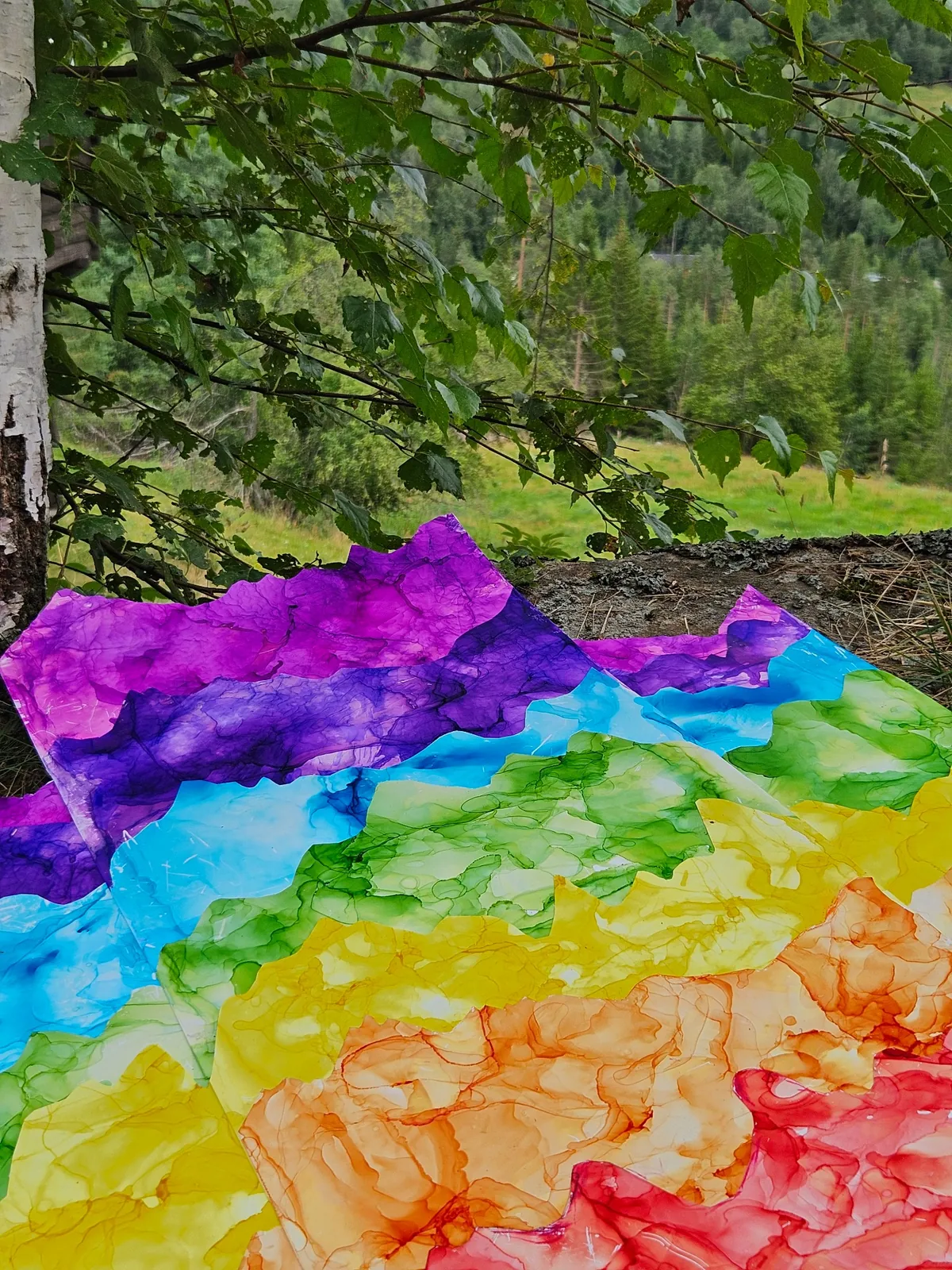 Regnbuefarget akvarellkunstverk med fjellformer i naturen under bjørketrær