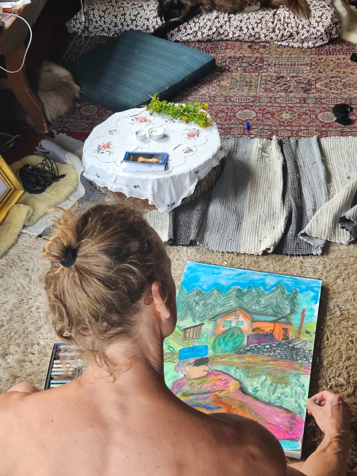 Kunstner som tegner fargerikt bilde av hus med furutrær i koselig rom