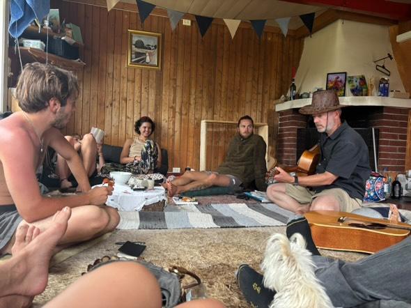 Koselig musikksamling i stuen med gitarspill, vimpler og venner samlet rundt på tepper